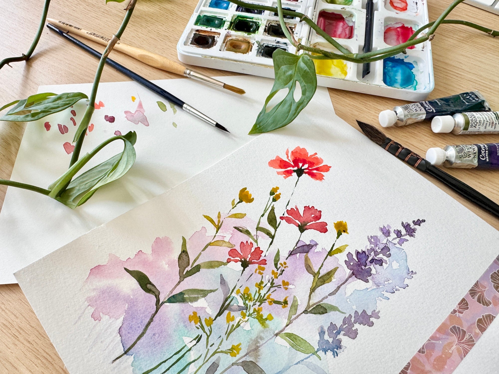 Aquarell Blumen Bild mit Malutensilien drum herum.